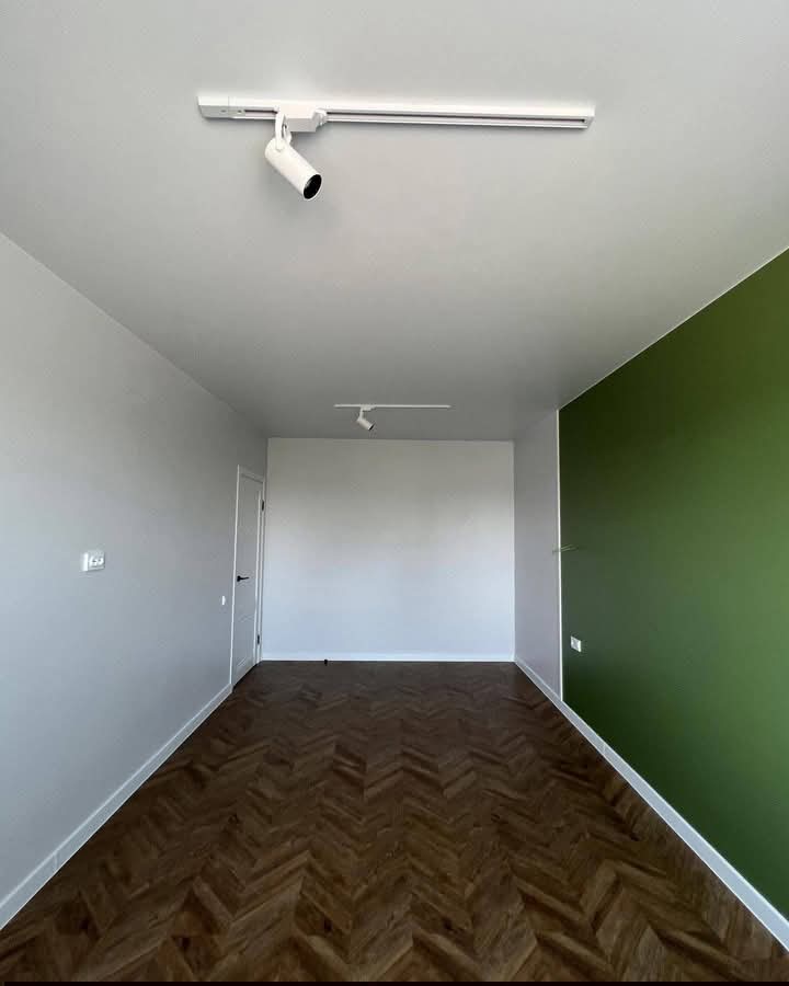 Chambre minimaliste avec mur vert et parquet sombre
